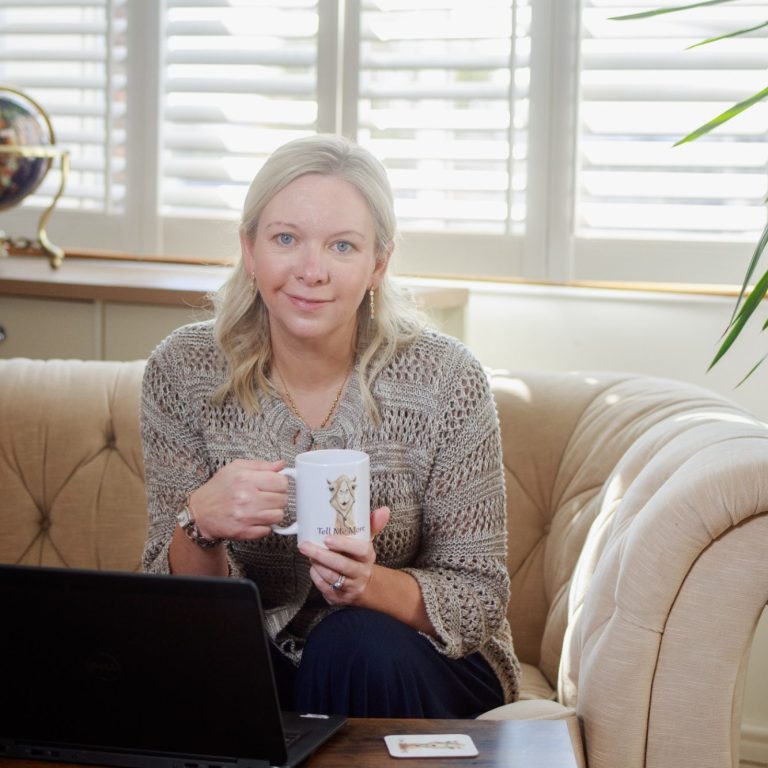 Woman holding a mug, sitting on a sofa with a laptop and plants in a sunny room.
