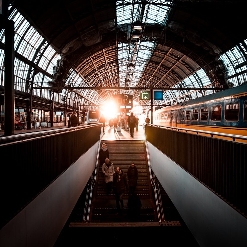 Illuminated train station entrance with commuters descending stairs and a train in the background.